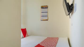 A single bed with a white mattress and a red and white patterned blanket. A calendar is mounted on the wall above the bed.