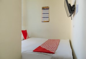 Una cama individual con un colchón blanco y una colcha estampada en rojo y blanco. Un calendario está colgado en la pared sobre la cama.