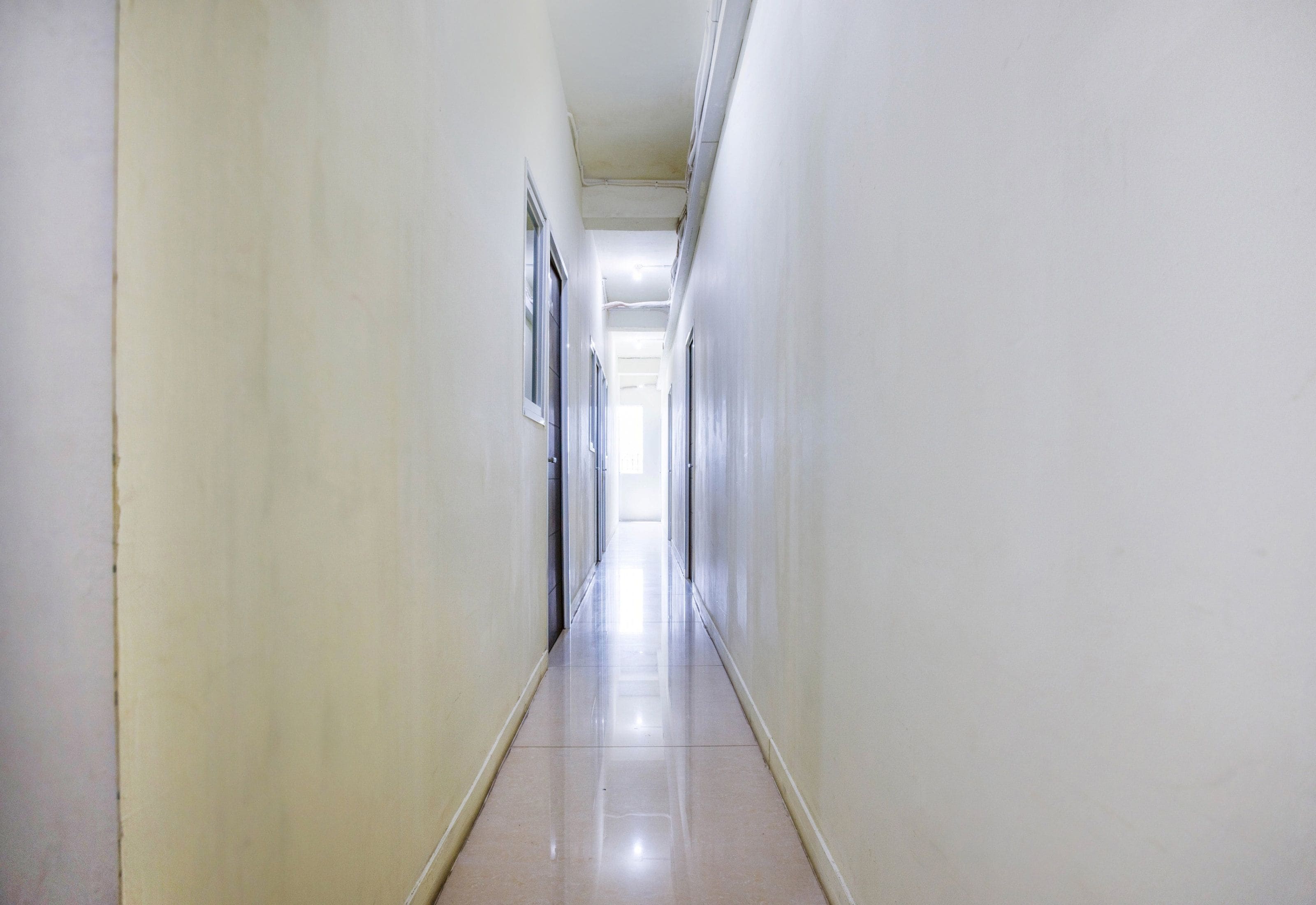A long, narrow hallway with white walls and a shiny tiled floor.