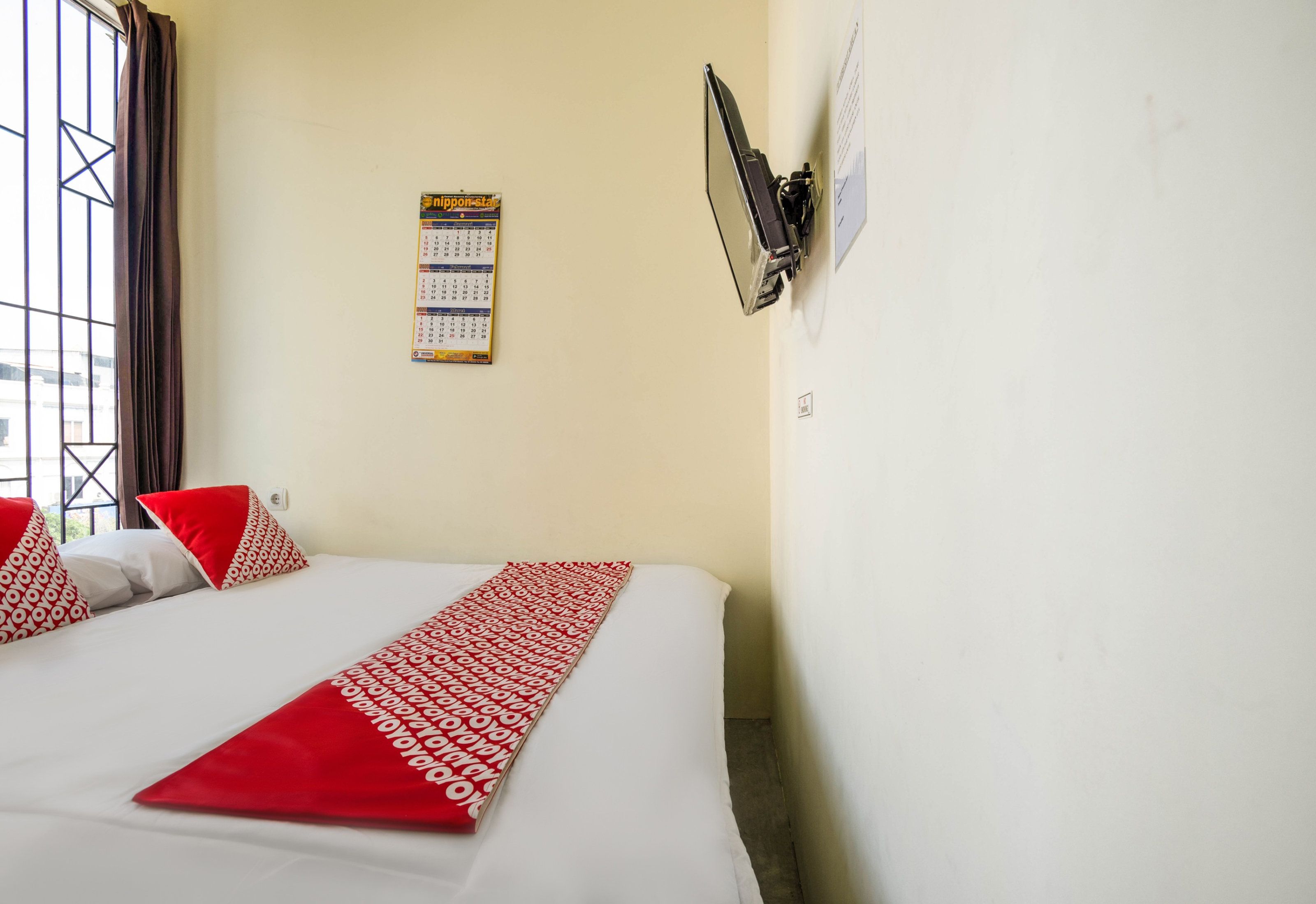 Habitación de hotel con cama, calendario, ventana con cortinas y aire acondicionado de pared.