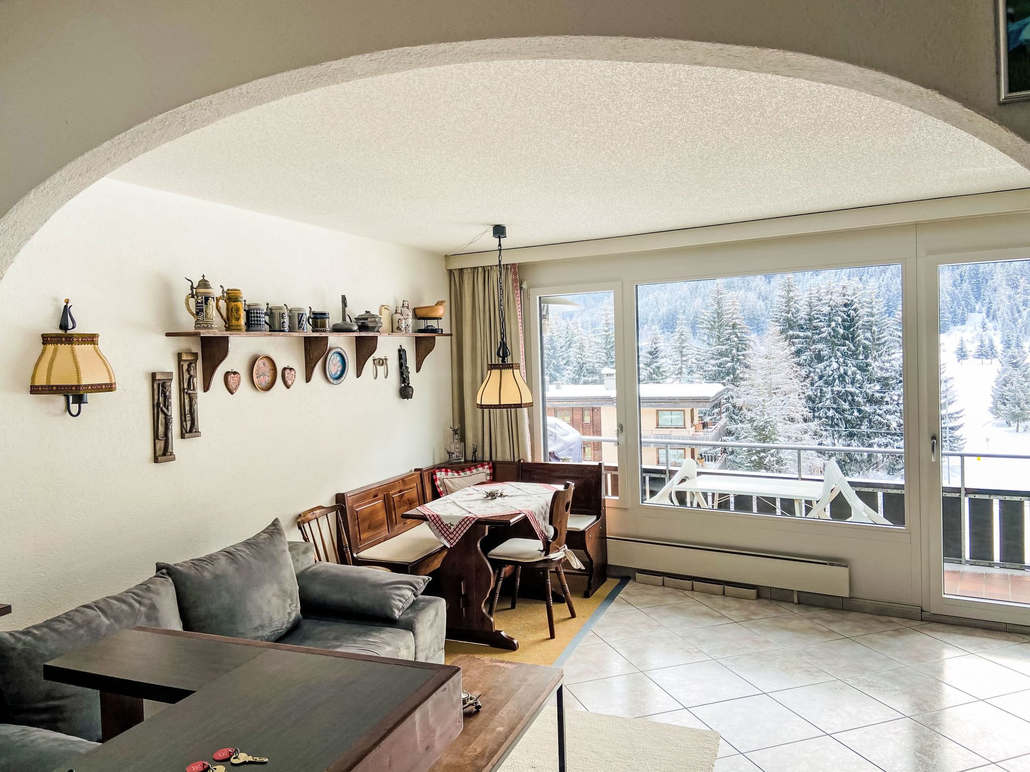 Una sala de estar acogedora con un sofá, una mesa de comedor y un balcón con vistas a árboles nevados.