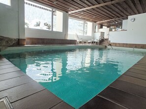 An indoor swimming pool with clear water, wooden deck, and a view of the outdoors through large windows. - Golfresidenz by Interhome (Davos)