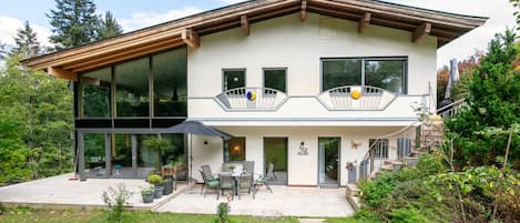 A modern two-story house with a balcony, a patio with outdoor furniture, and a stone pathway leading to the entrance.
