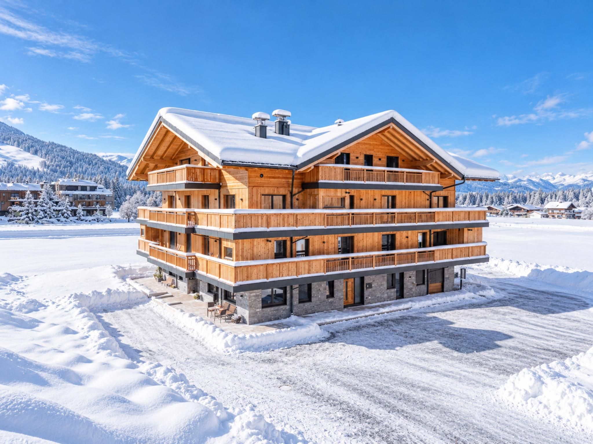 Eine mehrstöckige Holzlodge mit Balkonen, eingebettet in eine verschneite Landschaft mit Bergen im Hintergrund.