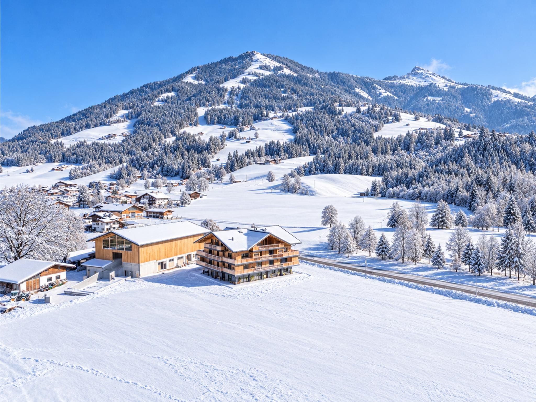Eine verschneite Berglandschaft mit einer Lodge mit mehreren Etagen und einer Skipiste im Hintergrund.
