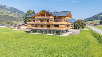 Ein mehrstöckiges Holzgebäude mit Balkonen, eingebettet in eine grüne Landschaft mit Hügeln im Hintergrund.