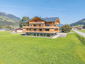 Ein mehrstöckiges Holzgebäude mit Balkonen, eingebettet in eine grüne Landschaft mit Hügeln im Hintergrund.