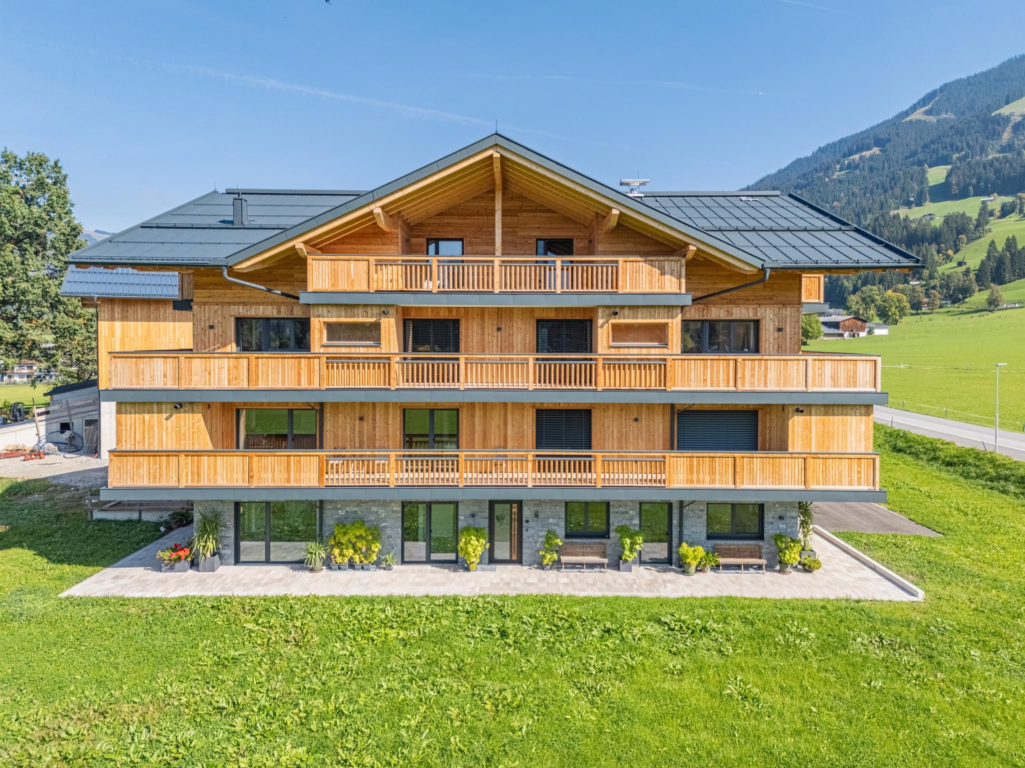 Un edificio de madera de varios pisos con balcones, situado en un paisaje verde con montañas al fondo.