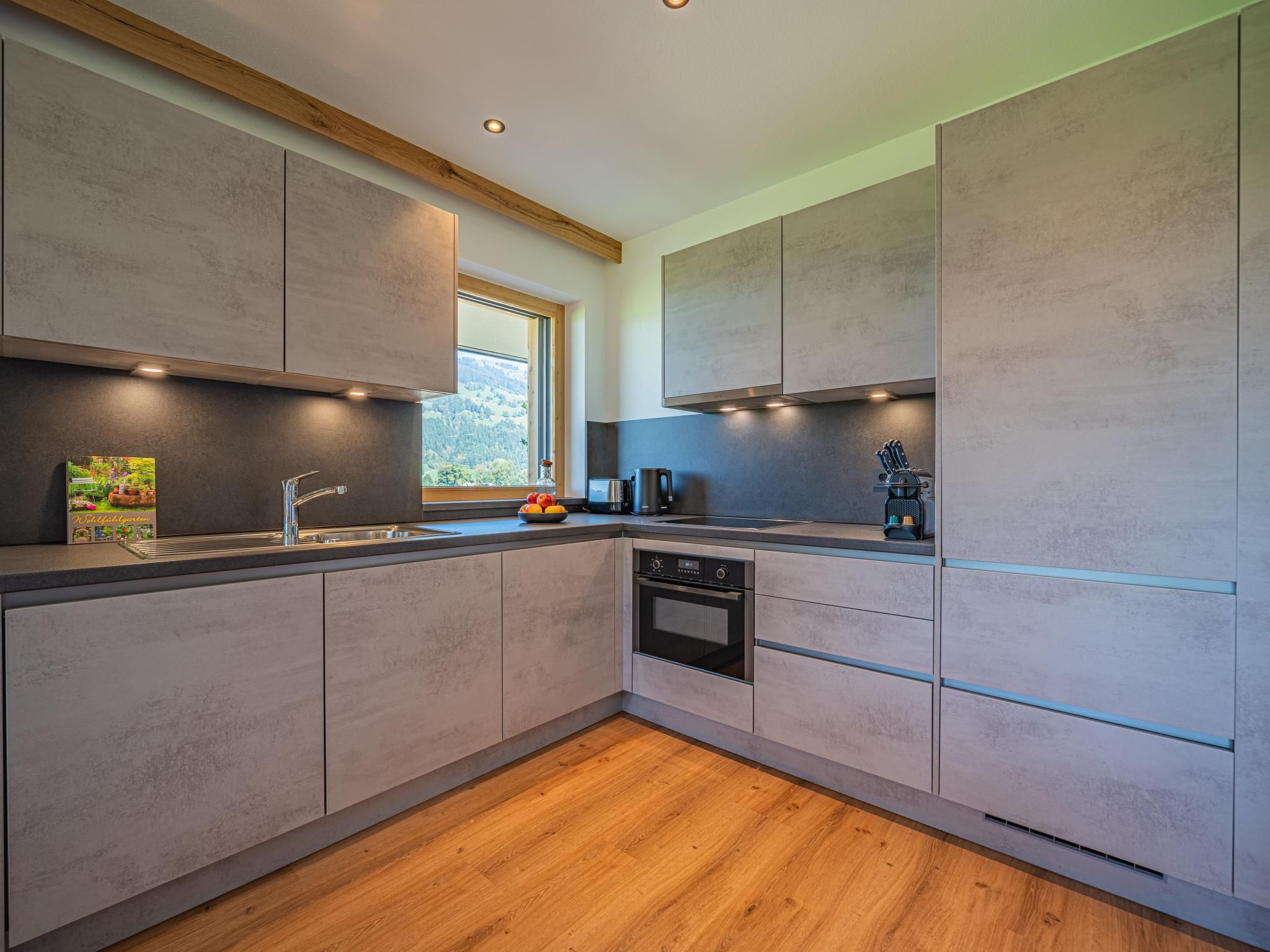 A modern kitchen with a built-in oven, a sink, and a window providing a view of the outdoors.