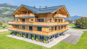 Eine mehrstöckige Holzhütte mit Balkonen, eingebettet in eine grüne Landschaft mit Bergen im Hintergrund.