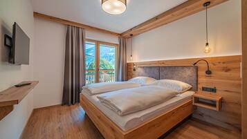 Ein Schlafzimmer mit einem Holzbett, einem an der Wand befestigten Fernseher und Blick ins Freie.