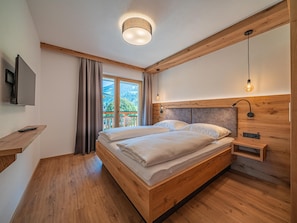 Ein Schlafzimmer mit einem Holzbett, einem an der Wand befestigten Fernseher und Blick ins Freie.