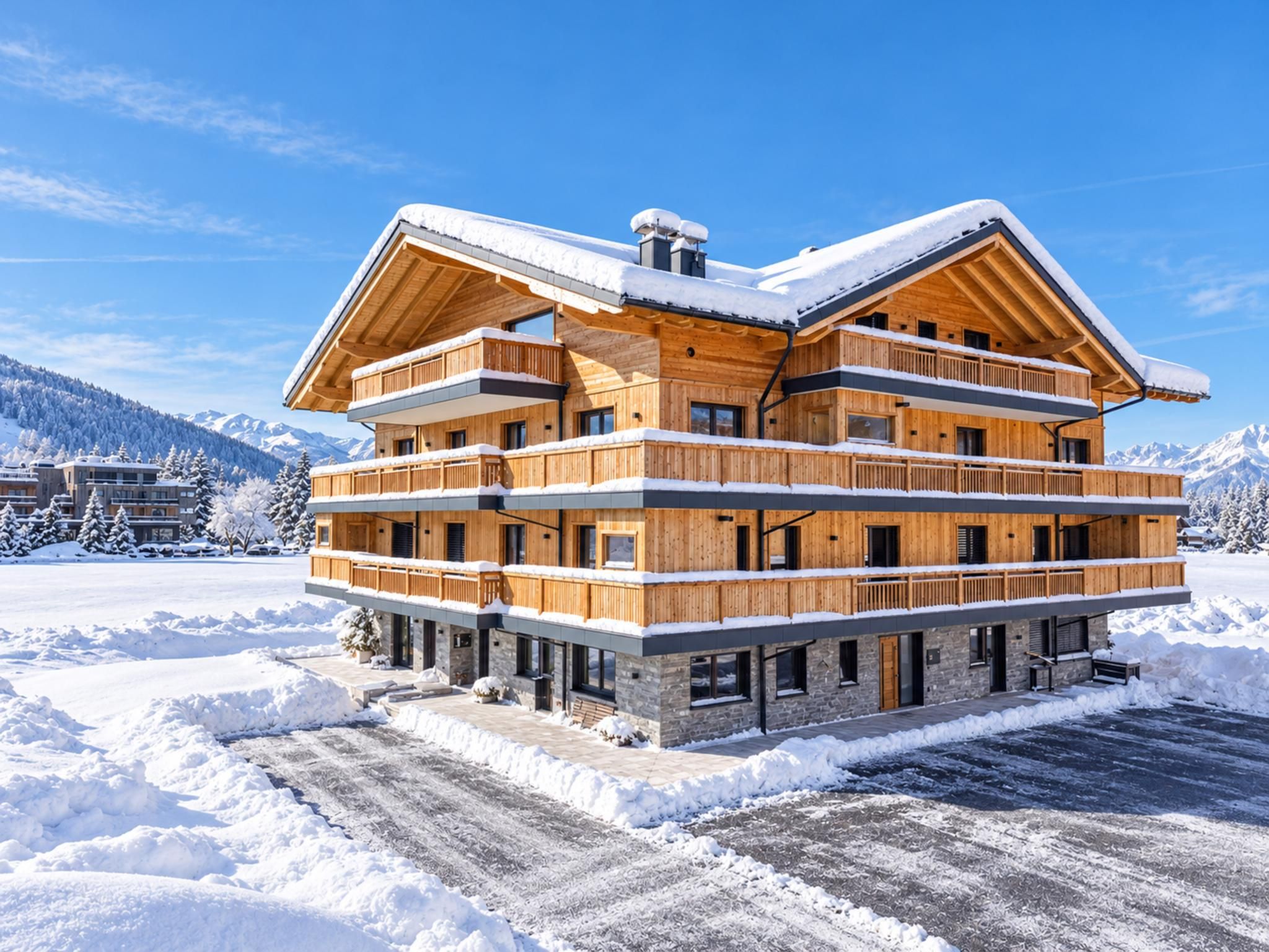 Ein mehrstöckiges Holzchalet mit Balkonen, eingebettet in eine verschneite Winterlandschaft mit Bergen im Hintergrund.