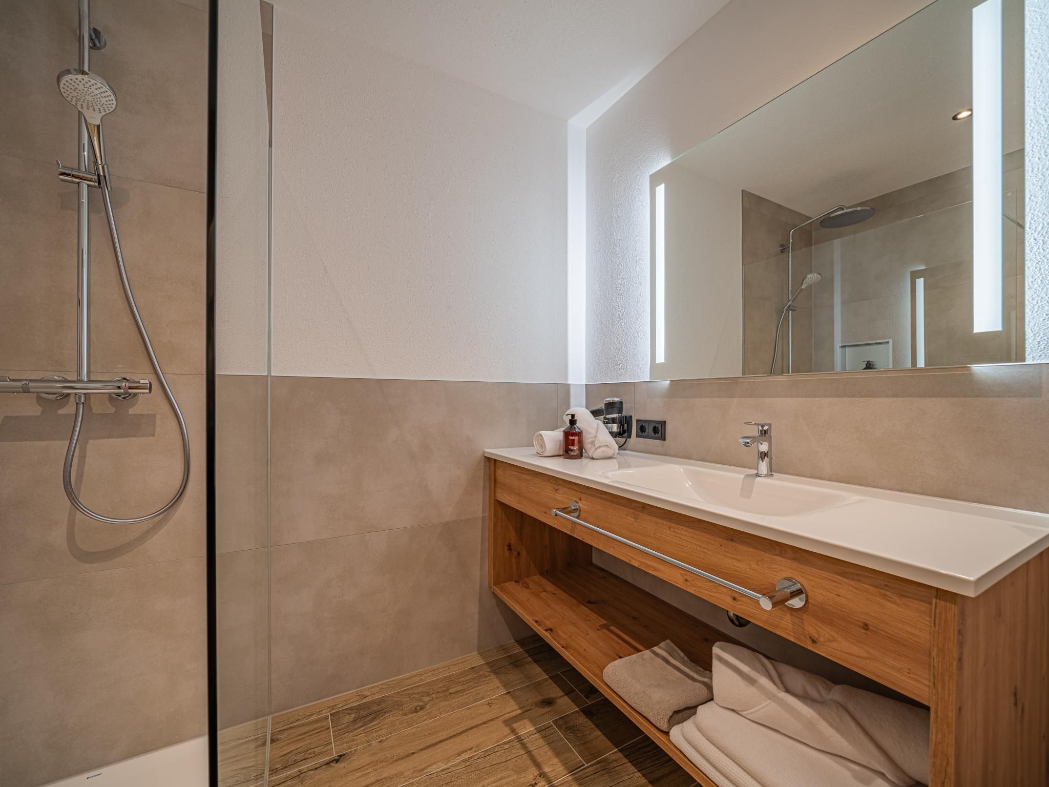 Ein modernes Badezimmer mit einer Duschkabine, einem Holzbadezimmermöbel mit Waschbecken und einem großen Spiegel.