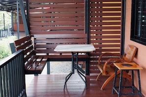 A wooden bench and table set on a porch with a view of a building. - Kittipoom Hill (Nopphitam)
