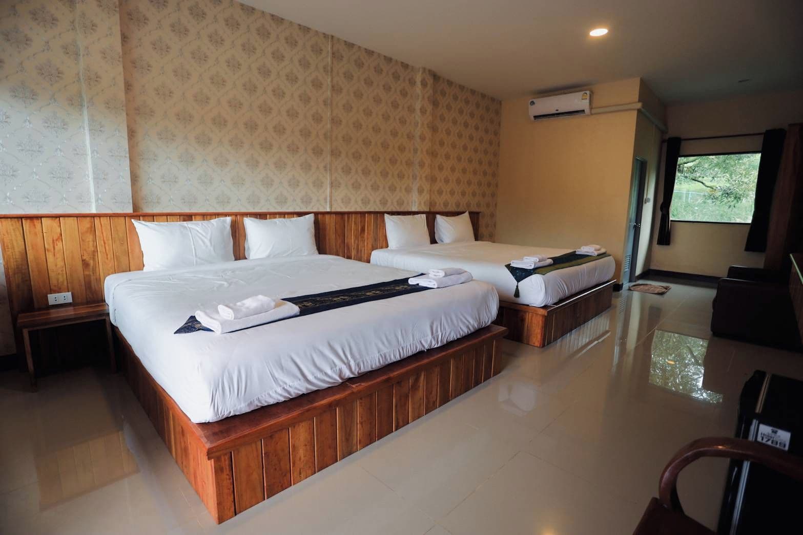 A hotel room with two beds, a wooden headboard, a nightstand, and a window with curtains.