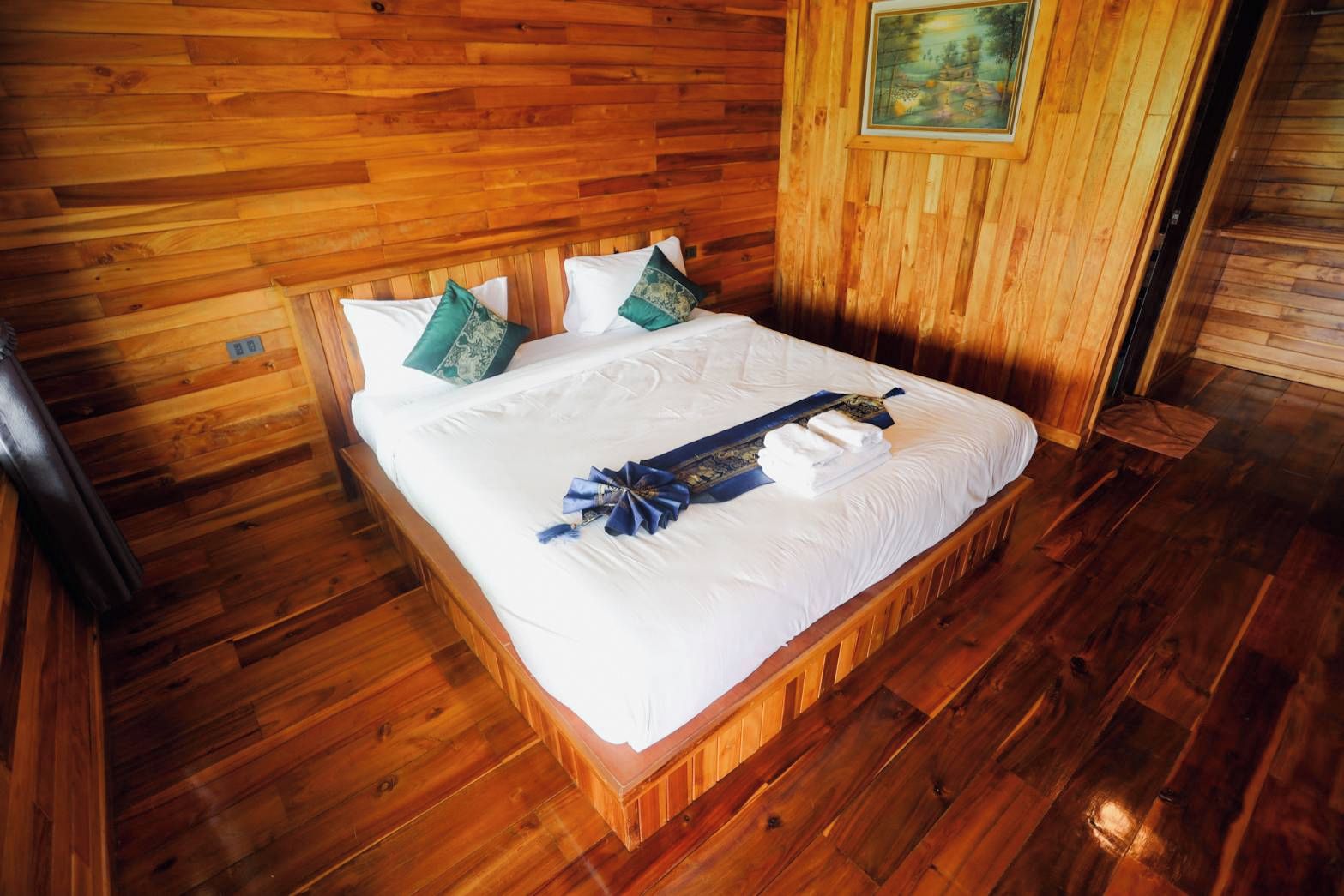 A wooden-paneled room with a bed, pillows, and a painting on the wall.