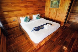 A wooden-paneled room with a bed, pillows, and a painting on the wall. - Kittipoom Hill (Nopphitam)