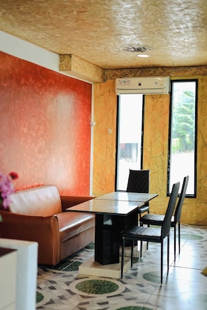 A room with a sofa, a dining table with chairs, a large window, and an air conditioning unit.