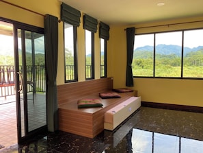 A room with a wooden bench, large windows, and a view of greenery.