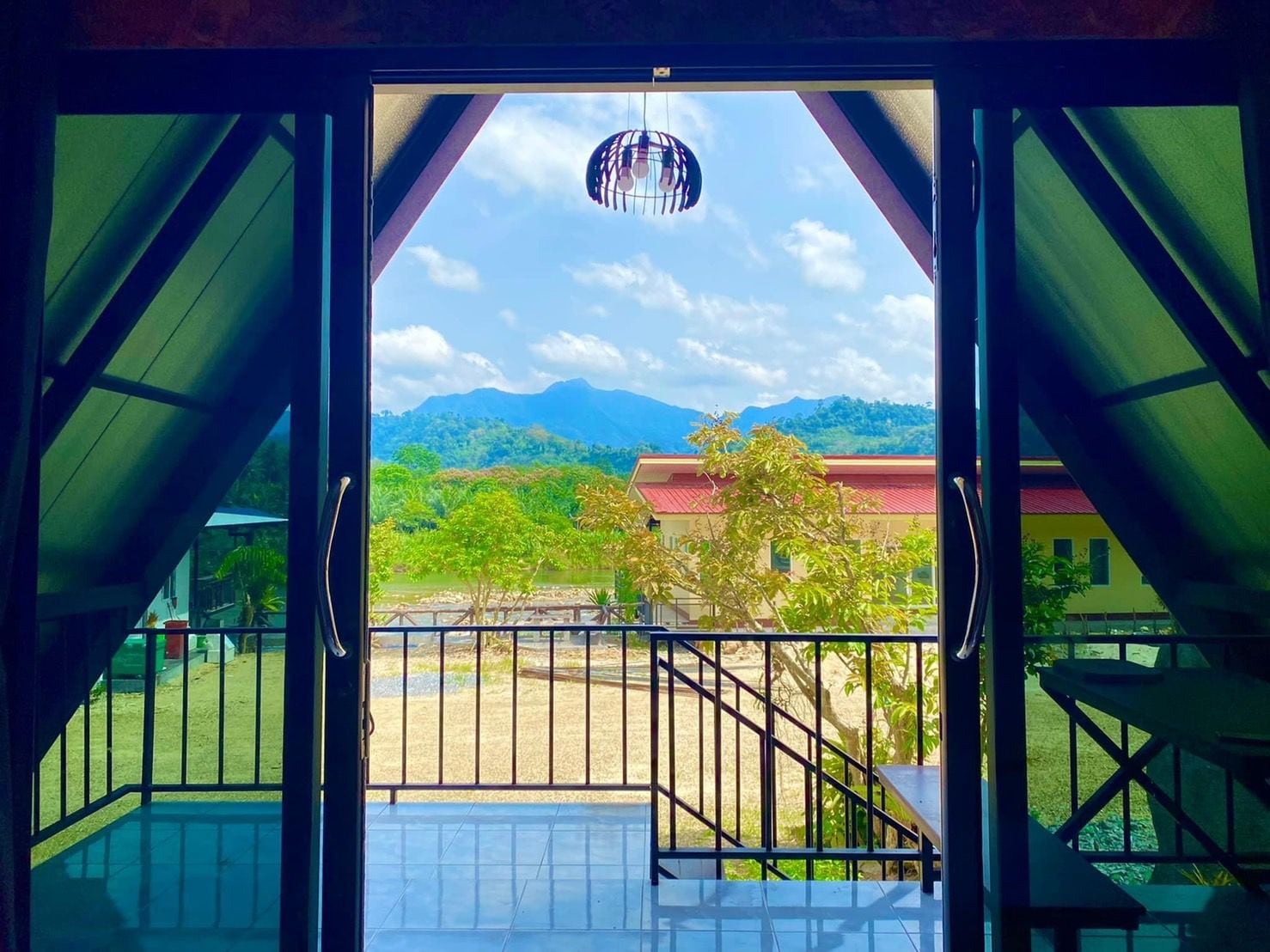 Un umbral abierto que da a un balcón con vistas a una cordillera y un edificio con techo rojo.