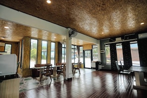 A spacious indoor area with a high ceiling, large windows, and a mix of seating arrangements. - Kittipoom Hill (Nopphitam)