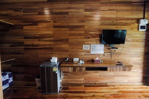 A wooden-paneled room with a reception desk, a refrigerator, a television mounted on the wall, and a small trash bin. - Kittipoom Hill (Nopphitam)
