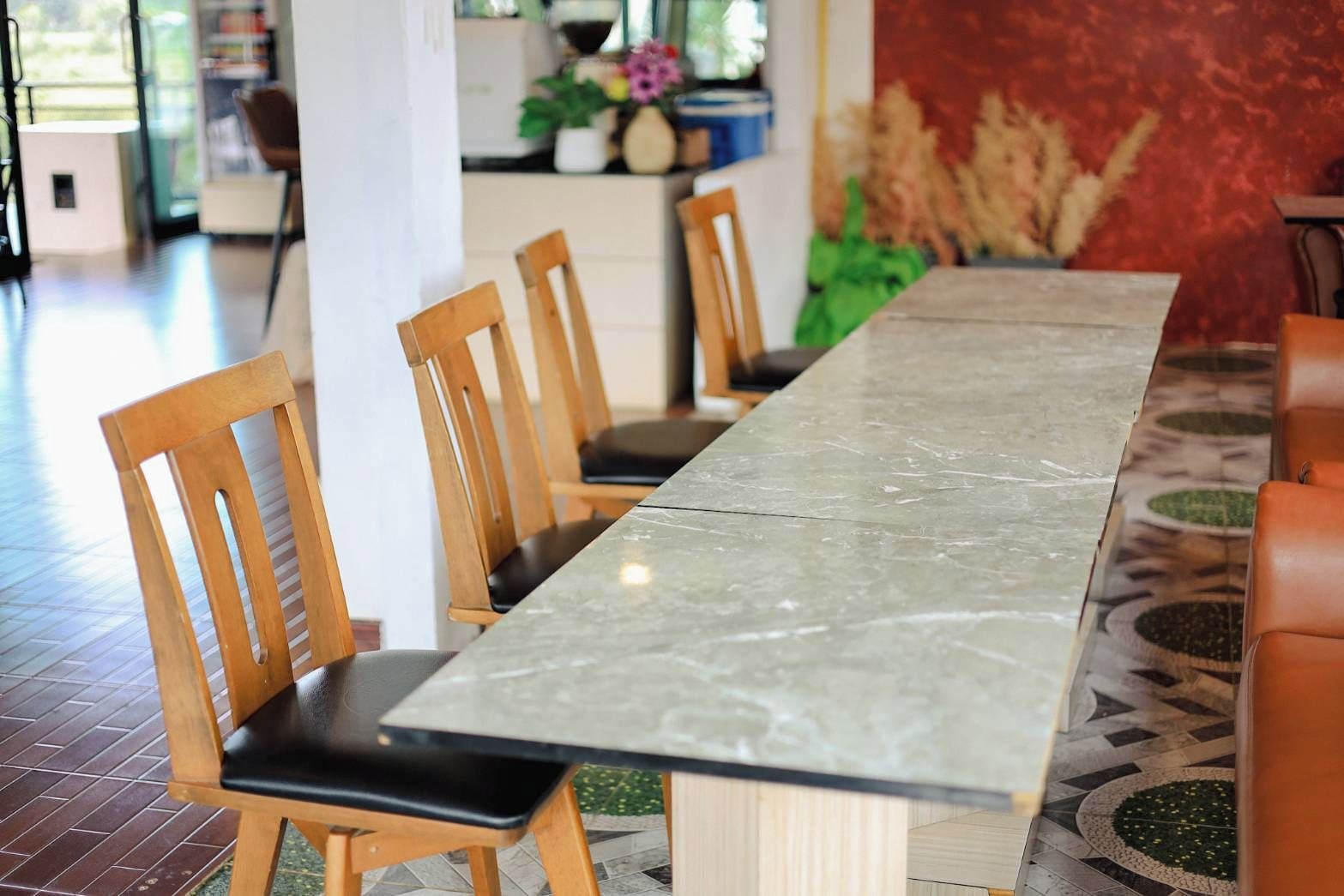 A long dining table with chairs, a patterned floor, and a red wall in the background.