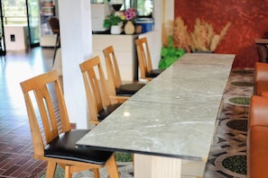 A long dining table with chairs, a patterned floor, and a red wall in the background.
