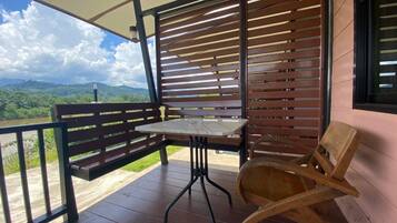A covered outdoor seating area with a table and chairs, overlooking a scenic landscape.