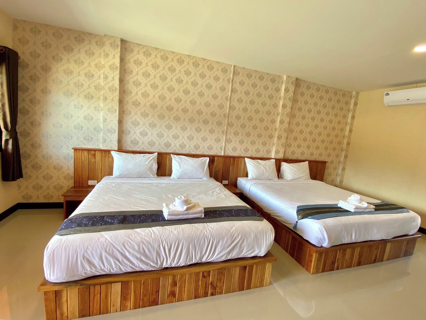 A hotel room with two beds, wooden headboards, and a patterned wallpaper.