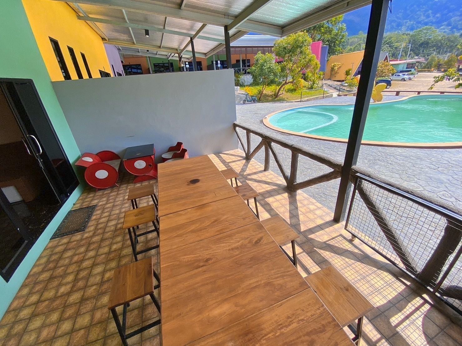 An outdoor seating area with a wooden table and chairs, a pool in the background, and a view of the surrounding area.