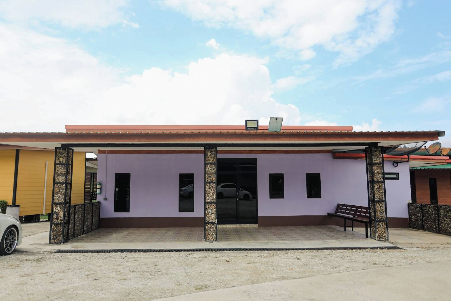 A building with a covered entrance, a bench, and a car parked outside.
