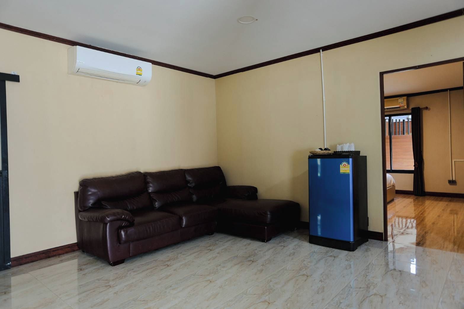 A room with a dark brown leather sofa, a blue refrigerator, and a white air conditioning unit on the wall.