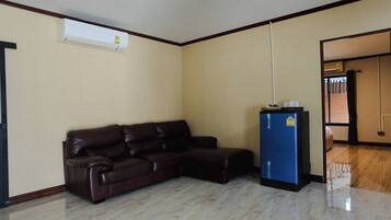A room with a dark brown leather sofa, a blue refrigerator, and a white air conditioning unit on the wall.