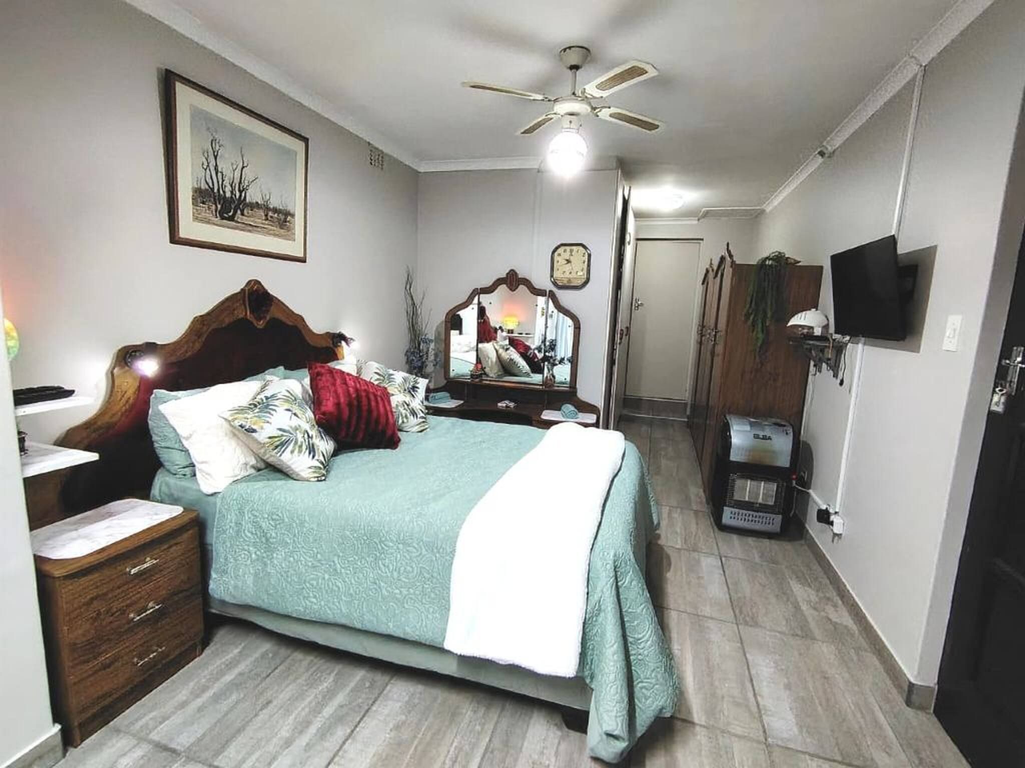 Un dormitorio con cama, mesita de noche, espejo, ventilador de techo, reloj, televisor y armario.