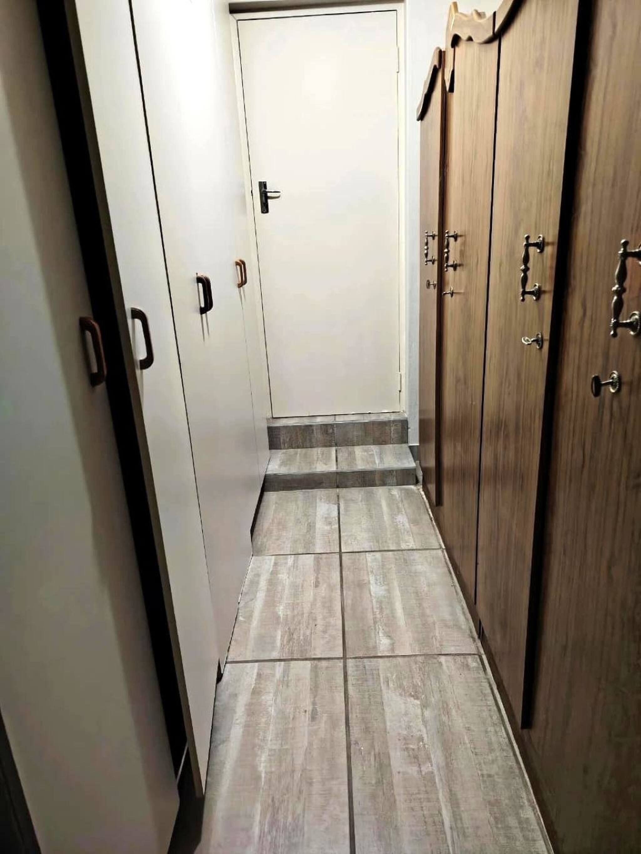 Un couloir étroit, avec une porte en bois au fond, bordé de meubles blancs dont les poignées sont noires.