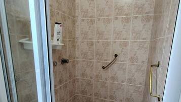 A shower with a glass door, a handheld showerhead, a towel rack, and a step with a non-slip surface.