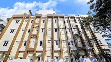 Un immeuble résidentiel à plusieurs étages, doté d’une façade symétrique, de climatiseurs et d’une entrée sécurisée par un portail.