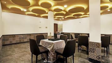 Un espace repas doté d’un plafond haut, agrémenté d’un éclairage encastré circulaire, d’une table centrale entourée de chaises et de carreaux muraux à motifs.