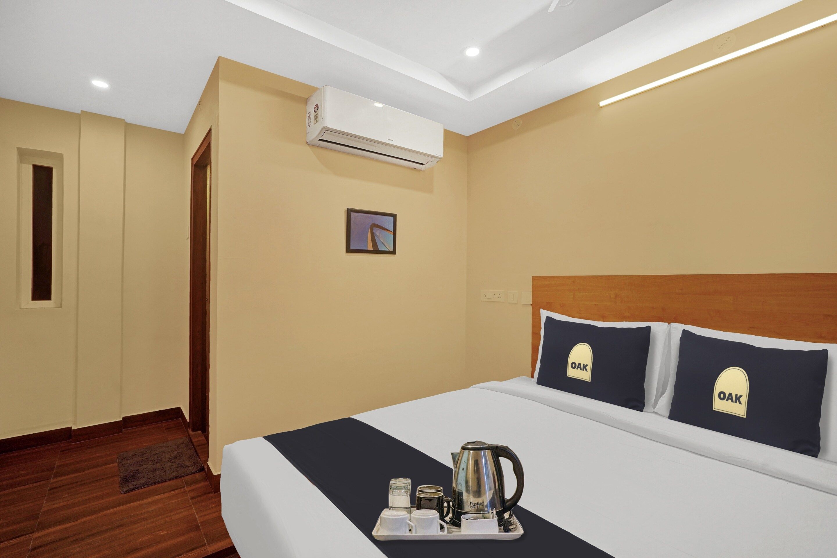A hotel room with a bed, a tray with a kettle and cups, an air conditioner, and a framed picture on the wall.