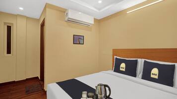 A hotel room with a bed, a tray with a kettle and cups, an air conditioner, and a framed picture on the wall.