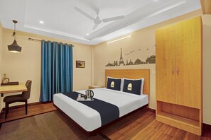 Una camera d'albergo con un letto, una scrivania, una sedia, un armadio e una ventola a soffitto.