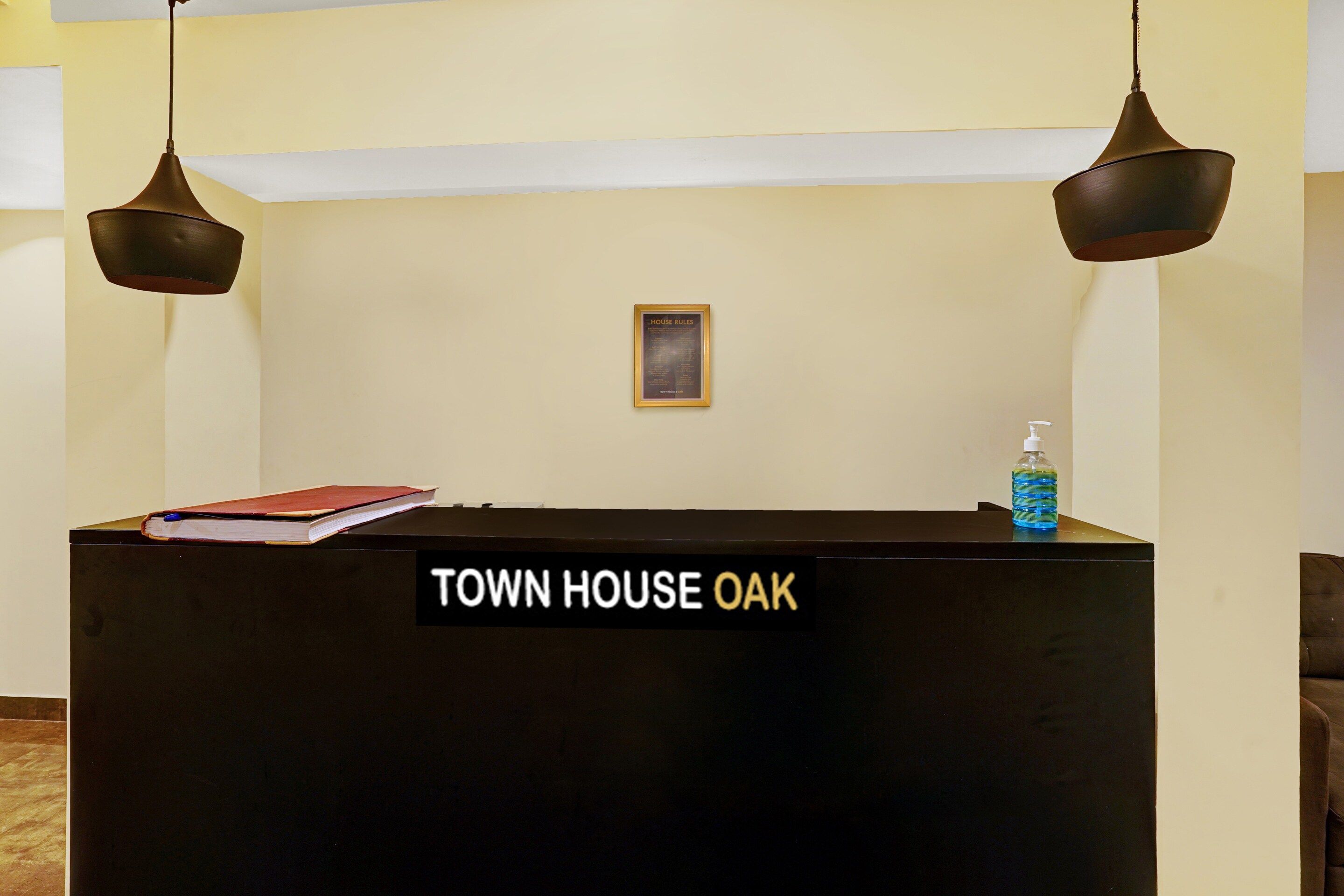 Una recepción con un cartel que dice 'TOWN HOUSE OAK' y un cartel enmarcado con las 'NORMAS DE LA CASA' encima.