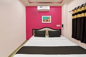 Una habitación con una cama, aire acondicionado de pared, un cuadro enmarco, un teléfono y una cortina.