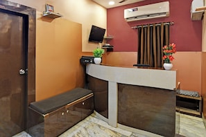 Zona de recepción con mostrador, banca, televisor, equipo de aire acondicionado y ventana con cortinas.
