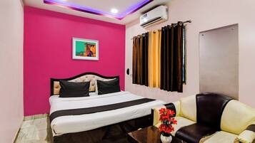Habitación de hotel con cama, sofá, mesa con un jarrón de flores, un cuadro en la pared y un equipo de aire acondicionado.