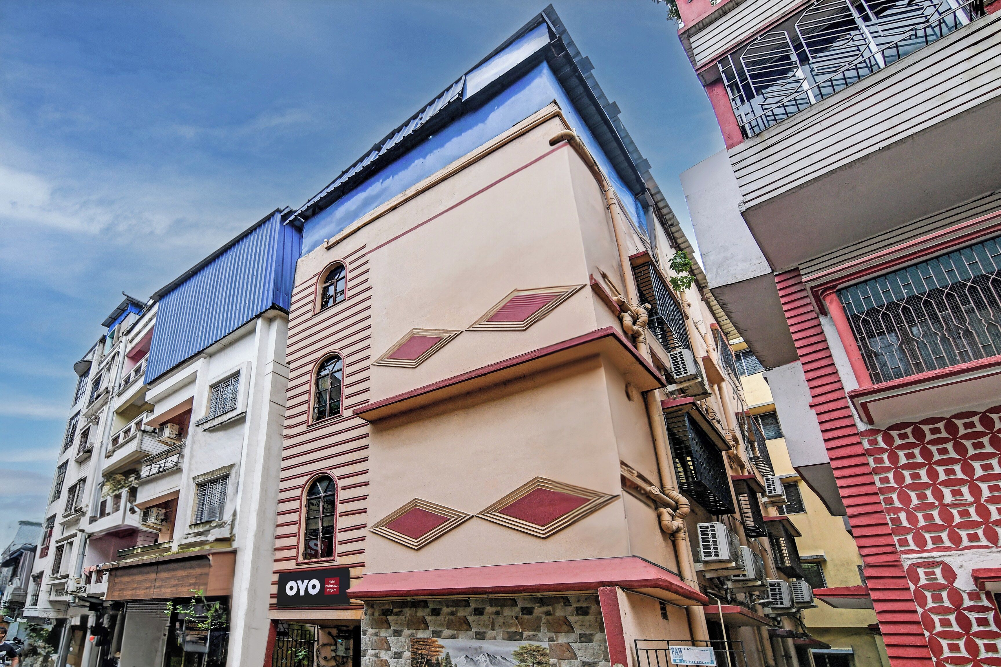 Un edificio de varios pisos con una mezcla de estilos arquitectónicos, destacando un techo azul y una fachada beige con patrones geométricos.