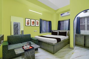 A room with a bed, a sofa, a small table with a tray, a window with curtains, and a wall-mounted air conditioner. - Hotel O Ecospace Business Park Kolkata (Kolkata)