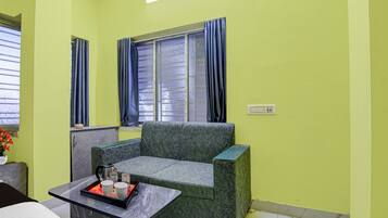 A room with a green wall, a window with curtains, a sofa, a small table with a tray, and a bed.